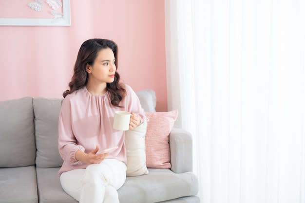 ソファに座ってコーヒーを飲む美しい若いアジアの女性