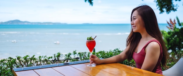 A beautiful young asian woman drinking juice while sitting and looking at the sea and blue sky view