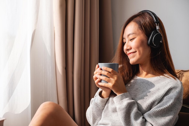 Una bella giovane donna asiatica si diverte a bere caffè e ad ascoltare musica con le cuffie a casa