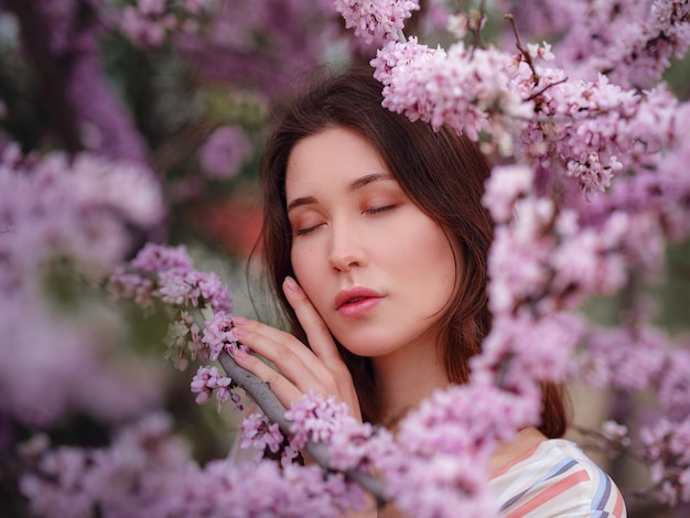 春に花が咲くのを楽しんでいる美しい若いアジアの女性。ヌードメイク。日本のように、春と花を祝う肖像画をクローズアップ