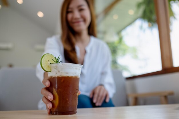 A beautiful young asian woman holding and grabbing a glass of iced coffee on the table