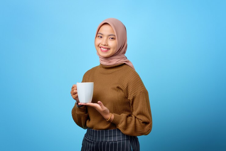 マグカップを保持し、青い背景でお茶を飲む美しい若いアジアの女性