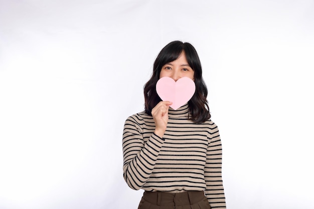 Beautiful young asian woman holding a paper heart while standing against white background Beautiful young asian woman with paper heart