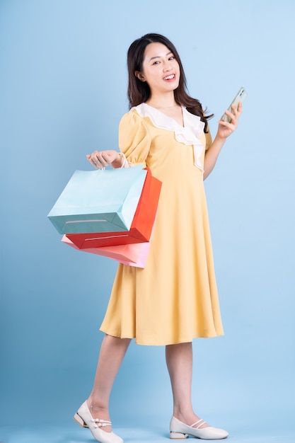 Beautiful young Asian woman holding shopping bag on blue background