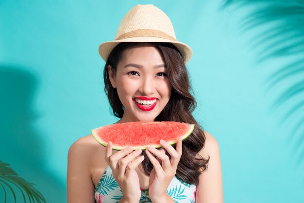 Beautiful young asian woman holding slice of watermelon and smiling