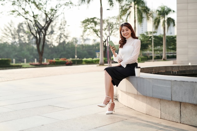 Beautiful young asian woman looking at her smartphone and smiling in urban