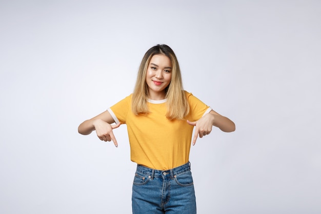 Beautiful young Asian woman point down to blank space on grey background.