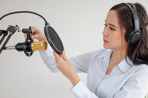 Foto bella giovane donna asiatica conduttrice radiofonica che lavora, indossa le cuffie, imposta il microfono, si prepara a parlare prima di registrare il podcast e vivere sui social media. in onda online in trasmissione in studio.