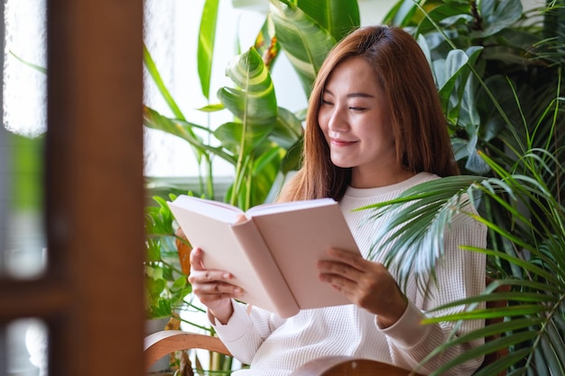 집에 화초 정원이 있는 발코니에서 책을 읽는 아름다운 젊은 아시아 여성