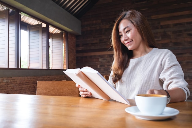 A beautiful young asian woman reading a book while drinking coffee