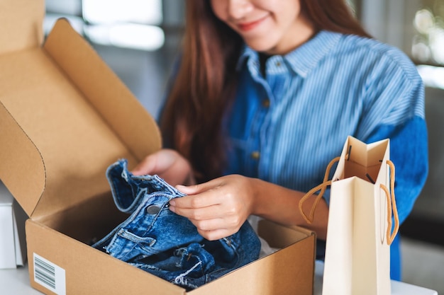 a beautiful young asian woman receiving and opening a postal parcel box of clothing at home for delivery and online shopping concept