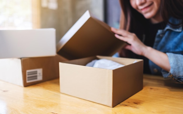 A beautiful young asian woman receiving and opening a postal parcel box at home for delivery and online shopping concept