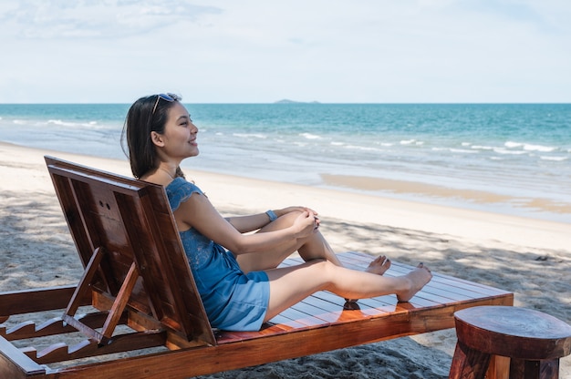 Beautiful young asian woman relaxing and sunbathing on wooden lounge on the beach in tropical sea