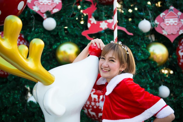 Bella giovane donna asiatica in vestiti di babbo natale all'apertola gente della thailandia ha inviato la felicità per i bambinibuon natalebenvenuto all'invernosfondo di natale decorato