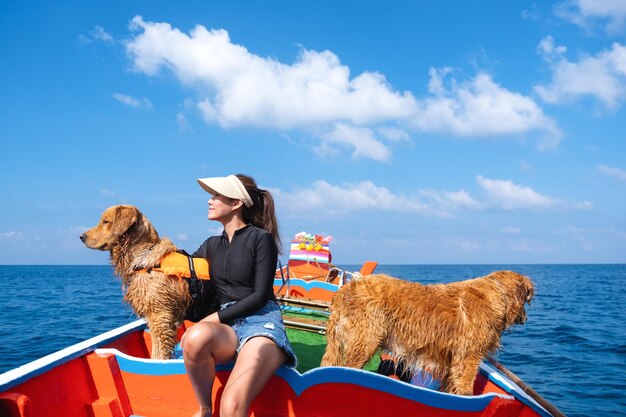 A beautiful young asian woman sitting on a boat and enjoying sailing on the sea with golden retriever dogs