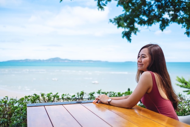 座って海と青い空を見ている美しい若いアジアの女性