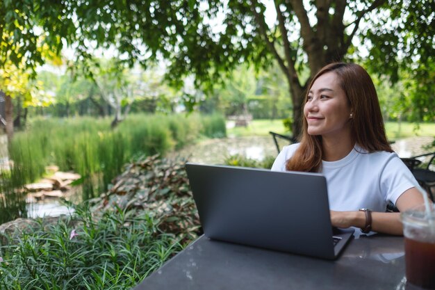 美しい若いアジアの女性は、公園でラップトップコンピューターでの作業から休憩します