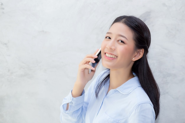 Beautiful young asian woman talking phone and smile standing on cement background.