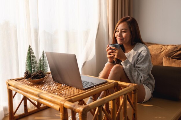 A beautiful young asian woman using and working on laptop computer while drinking coffee at home