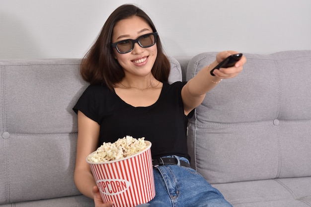 Beautiful young asian woman watching tv at home. eating\
popcorn. time at home