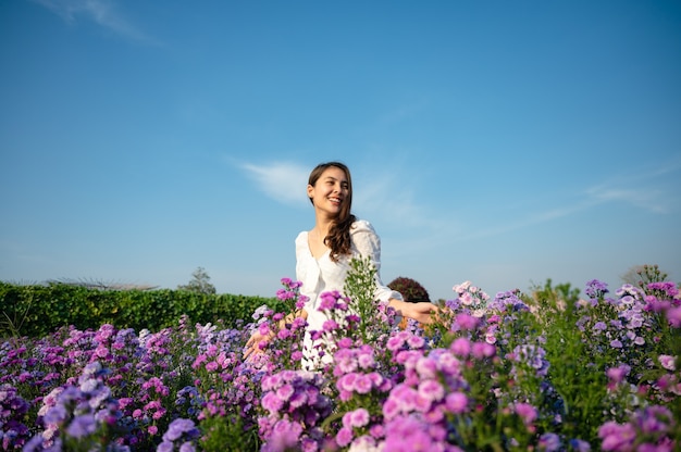 日当たりの良い庭に咲くマーガレットの花を楽しんでいる白いドレスの美しい若いアジアの女性