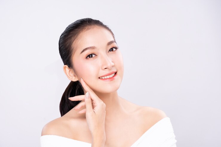 美しさできれいな新鮮な白い肌の顔を持つ美しい若いアジア女性は、指で肩に触れるポーズします。