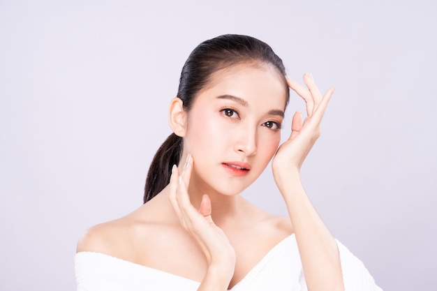 Beautiful Young Asian woman with clean fresh white skin face in beauty pose touching shoulder with finger.