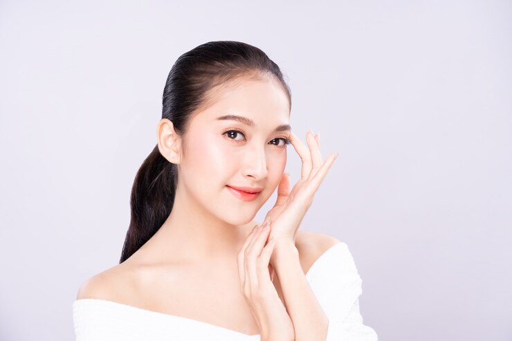 美しさできれいな新鮮な白い肌の顔を持つ美しい若いアジア女性は、指で肩に触れるポーズします。
