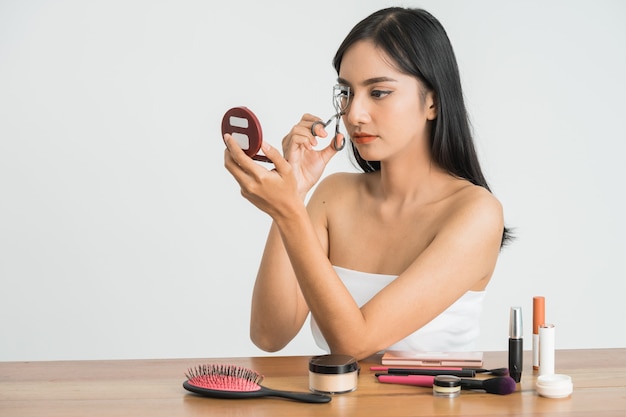 Beautiful young asian woman with eyelash curler on white wall