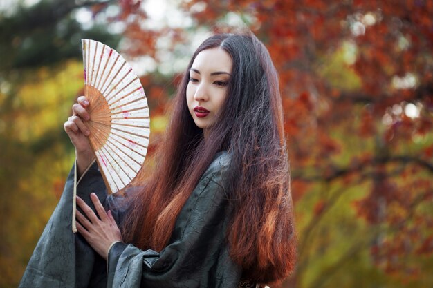 정원에서 팬을 가진 아름 다운 젊은 아시아 여자