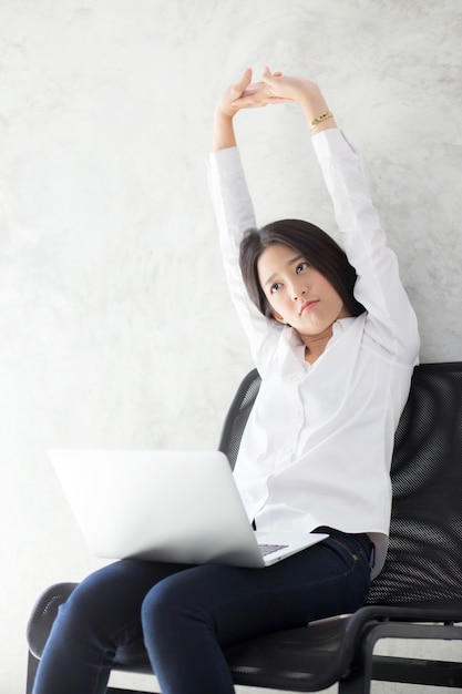 ラップトップストレッチと運動の美しい若いアジアの女性は、仕事の成功後にリラックスします。