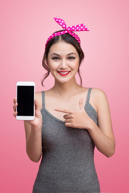 Beautiful young asian woman with pin-up make-up and hairstyle over pink background with mobile phone