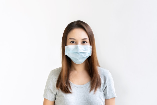 Beautiful young Asian woman with protective face mask on white wall