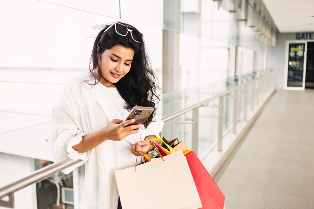 beautiful young asian woman with shopping bags using smartphone in mall