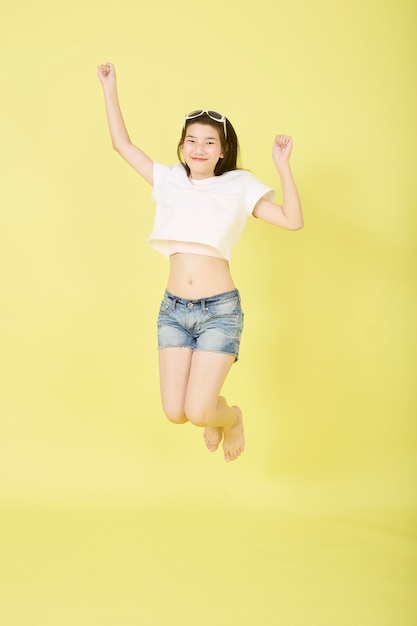 Beautiful young Asian women with sunglasses on her head jumping on yellow background