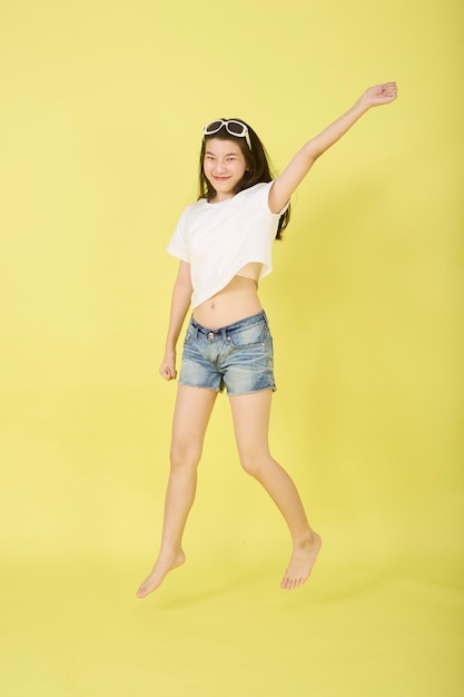 Beautiful young Asian women with sunglasses on her head jumping on yellow background