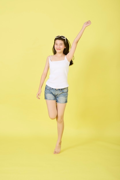 Beautiful young Asian women with sunglasses on her head jumping on yellow background