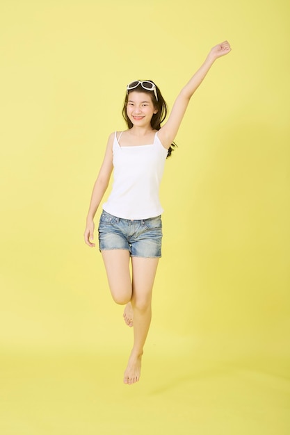 Beautiful young Asian women with sunglasses on her head jumping on yellow background