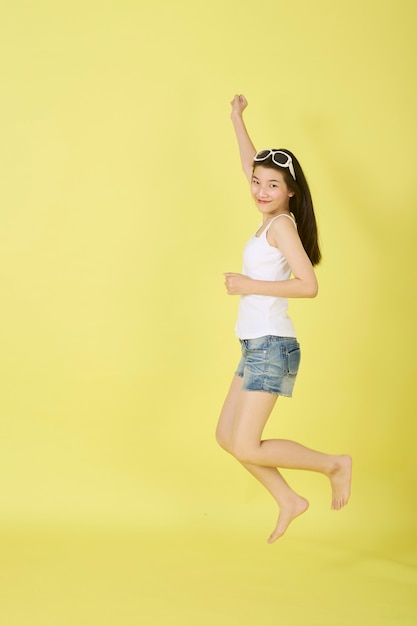 Beautiful young Asian women with sunglasses on her head jumping on yellow background