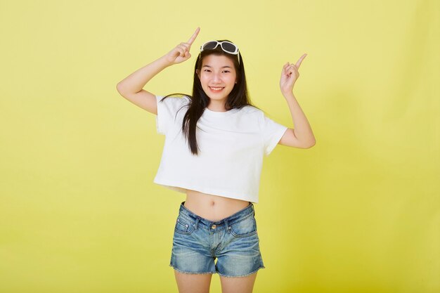 Beautiful young Asian women with sunglasses on her head pointing up on yellow background