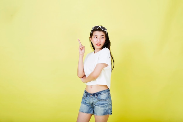 Beautiful young Asian women with sunglasses on her head pointing up on yellow background