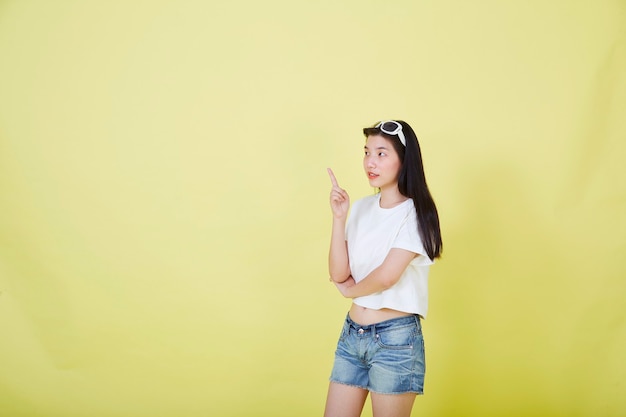 Beautiful young Asian women with sunglasses on her head pointing up on yellow background