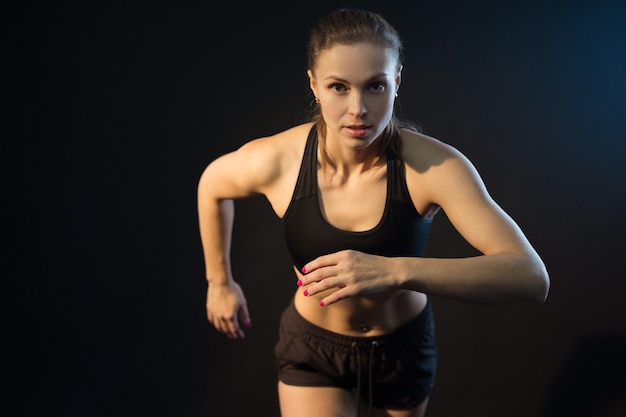 beautiful young athletic woman getting ready to run on a black background