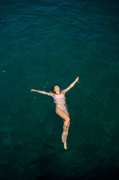 A beautiful young attractive woman in a swimsuit lies on the surface of the water at the sea. View from above. She is enjoying her vacation. Selective focus