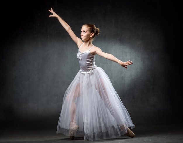 Beautiful young ballerina is dancing in the studio on a darkwallA little dancer. Ballet dancer.