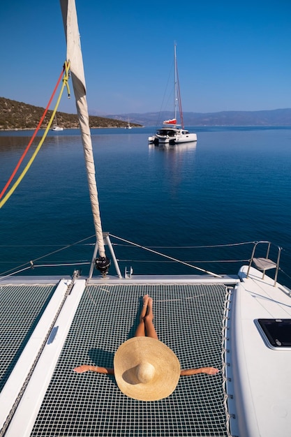 Beautiful young blond woman in bikini laying on catamaran bow\
at sunny summer day