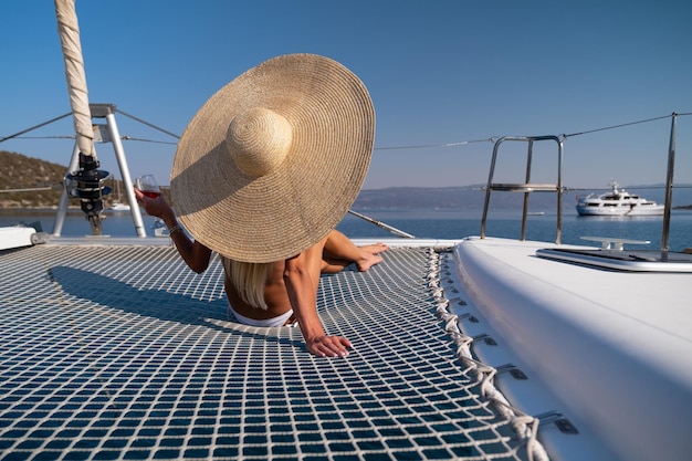 Beautiful young blond woman in bikini sitting on catamaran bow at sunny summer day