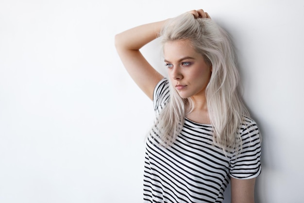 Foto bella giovane donna bionda in posa mentre si appoggia sul muro bianco