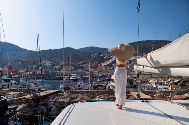 Beautiful young blond woman standing on catamaran at sunny summer day at Hydra marina bay Greece