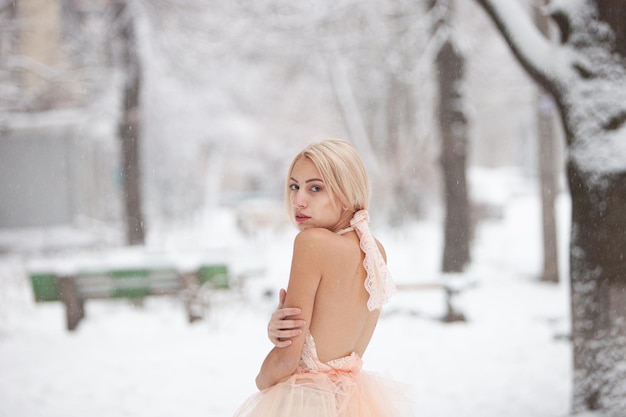 A beautiful young blond woman in a white dress posing in a snowy winter park. Soft focus. Selective focus